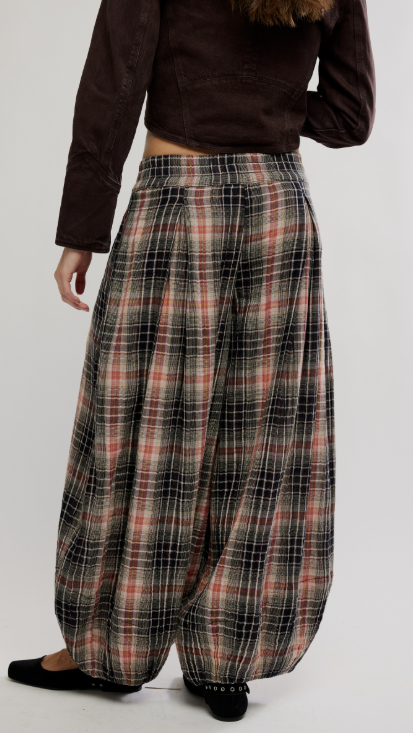Woman shown from behind wearing plaid balloon pants with brown jacket on white background