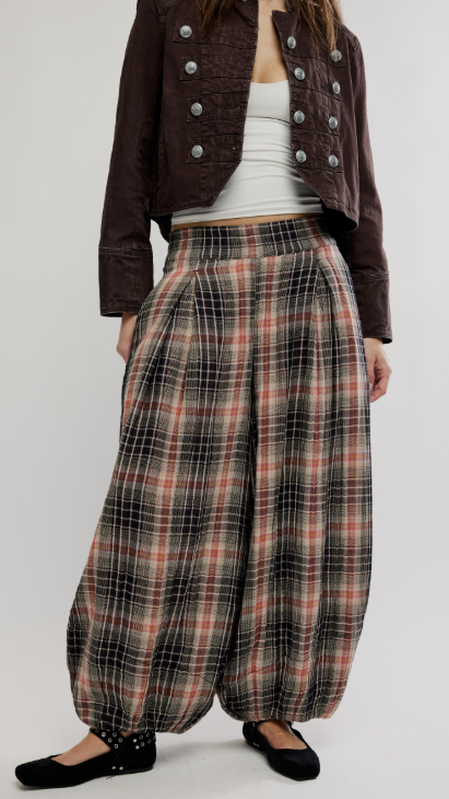 Woman wearing plaid balloon pants with brown jacket on plain background