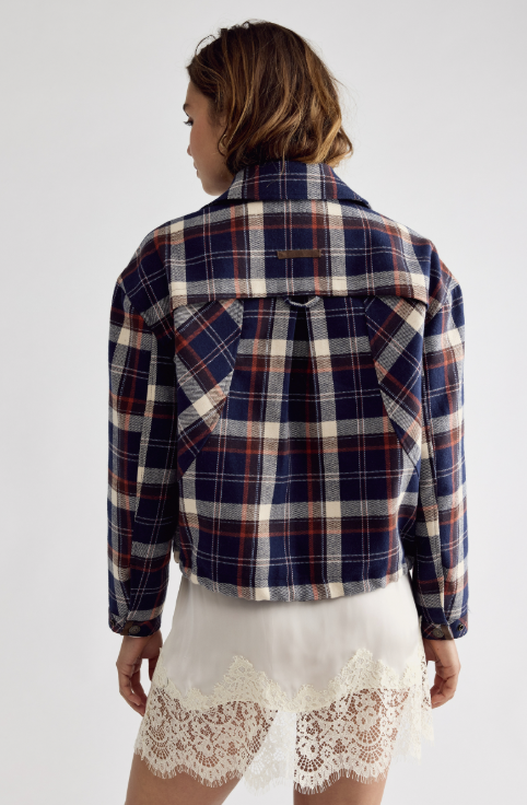 A woman shown from the back wearing a cropped plaid flannel shirt jacket in navy, red, and cream, paired with white lace-trimmed shorts against a light gray studio background.