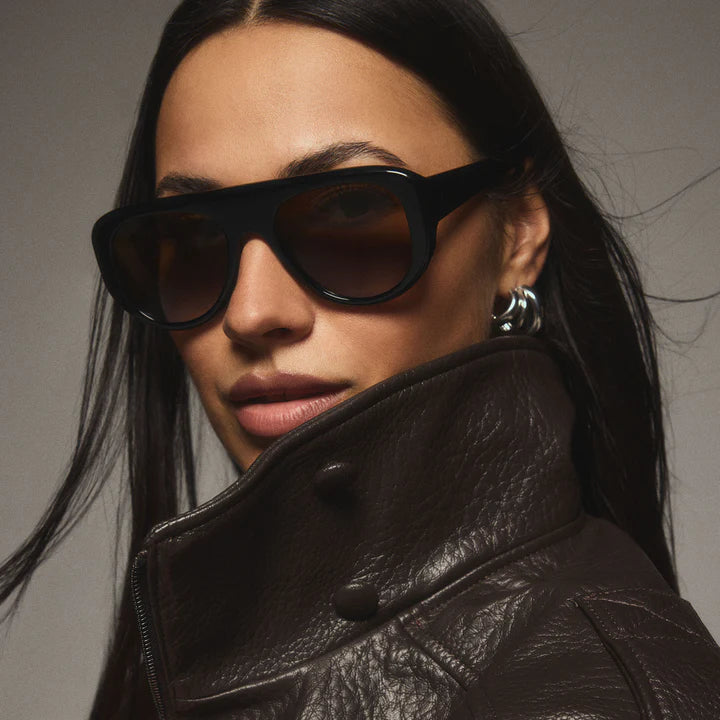 Woman wearing black sunglasses and a dark leather jacket against a gray background