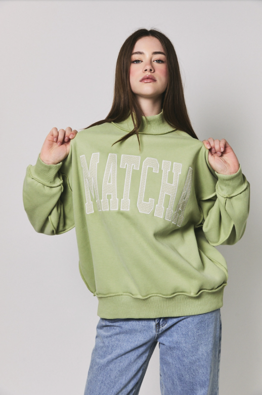 A woman modeling a sage green mock-neck sweatshirt with &
