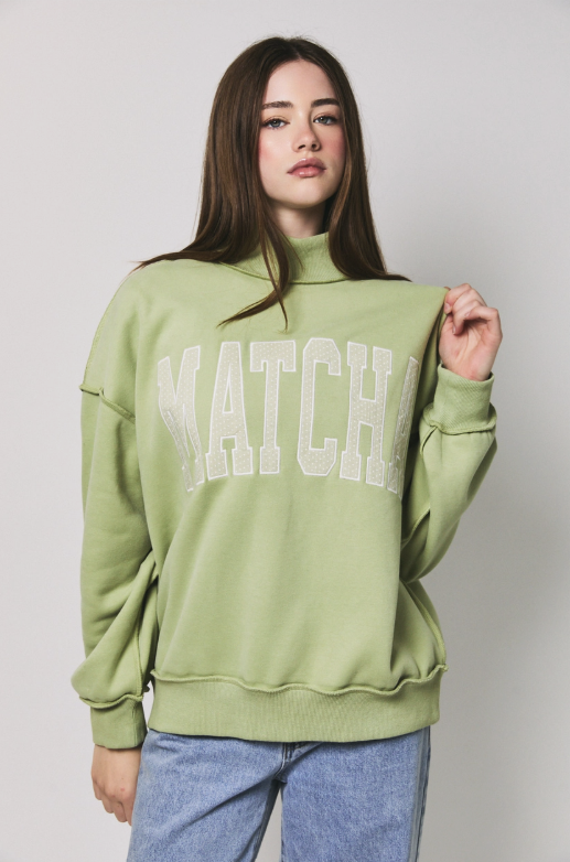 A woman modeling a sage green mock-neck sweatshirt with &