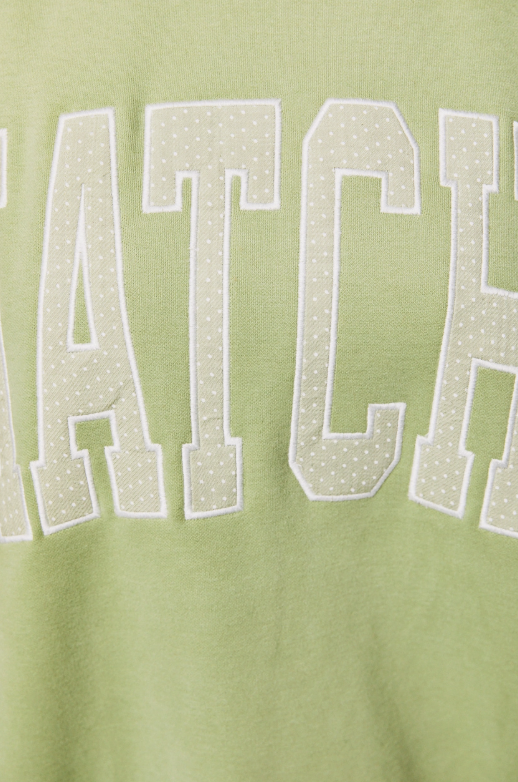 Close-up of a light green sweatshirt featuring large collegiate-style varsity letters outlined in white and filled with small white dots.