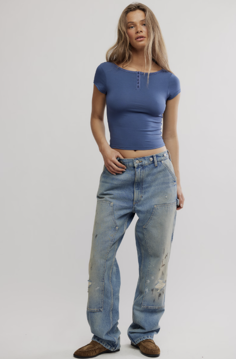 A woman modeling a blue short-sleeve crop top and light-wash distressed jeans against a plain light gray studio background.