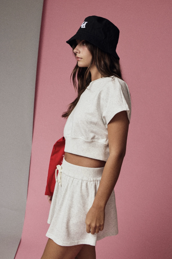 Woman wearing a white crop top and skirt with a black cap against a pink background
