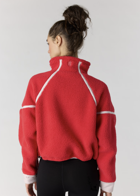 A woman shown from the back wearing a red cropped fleece pullover with white contrast piping and white ribbed cuffs, paired with black leggings, against a light gray studio background.