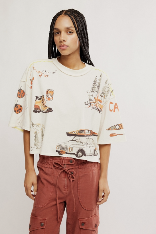 Woman wearing a graphic t-shirt with vehicle and nature prints on a plain background