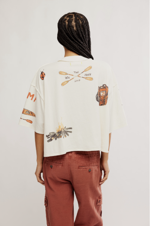 Person wearing a white t-shirt with graphic designs on the back and brown pants, standing against a plain background.