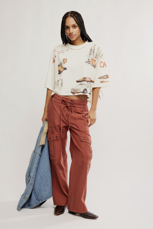Woman wearing a patterned crop top and rust-colored pants with a denim jacket on a white background