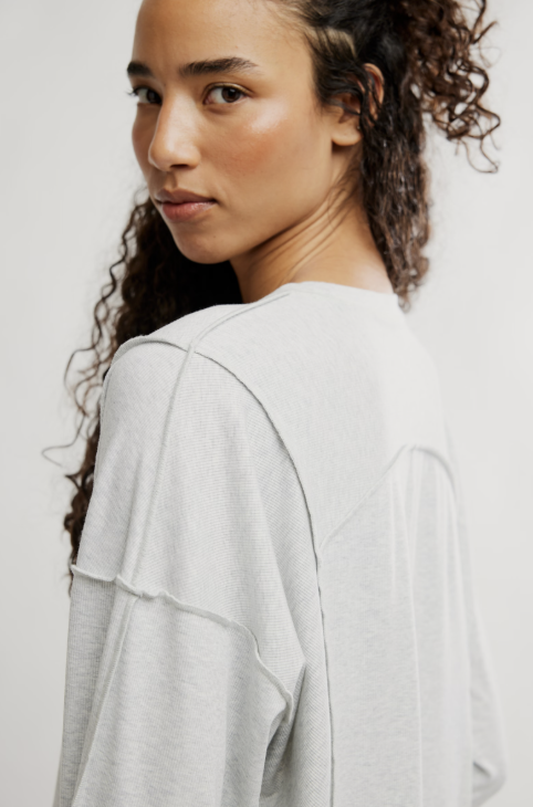 A close-up shot of a model wearing a light gray oversized long-sleeve top, showing the back and shoulder details against a plain light background.