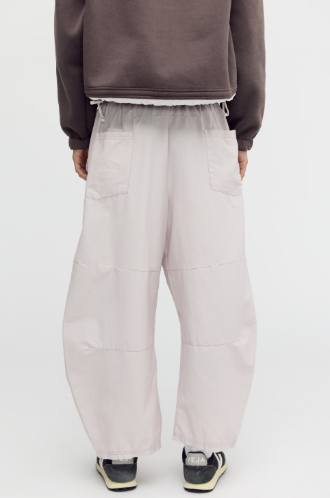 Woman shown from back wearing beige pants with brown jacket on white background