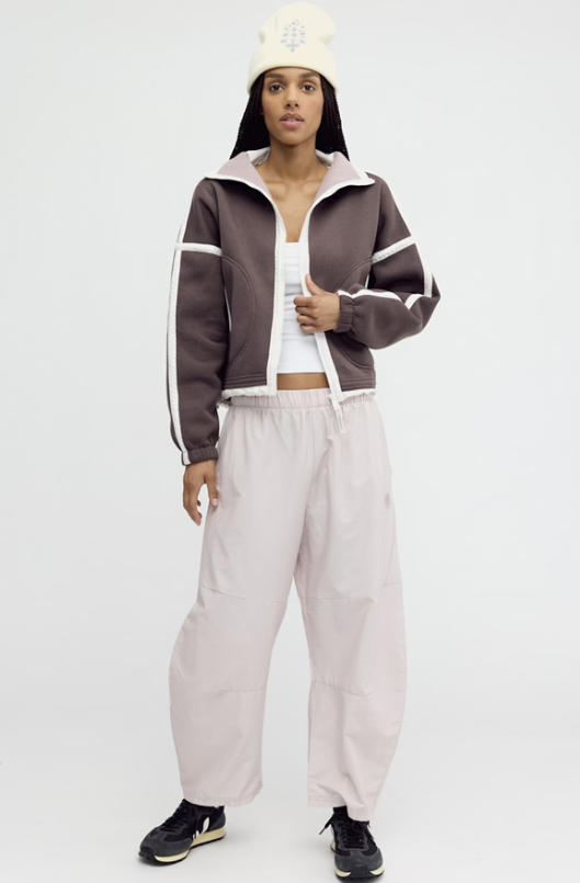 Woman modeling beige pants and brown jacket with ivory beanie on white background