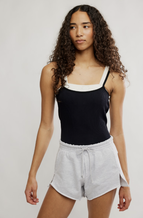 Woman wearing black tank and grey shorts on plain background