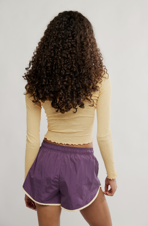 Woman shown from back wearing purple shorts and yellow top on white background