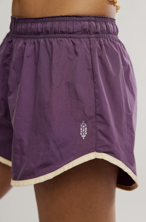 Close up of woman wearing purple shorts with yellow logo on white background