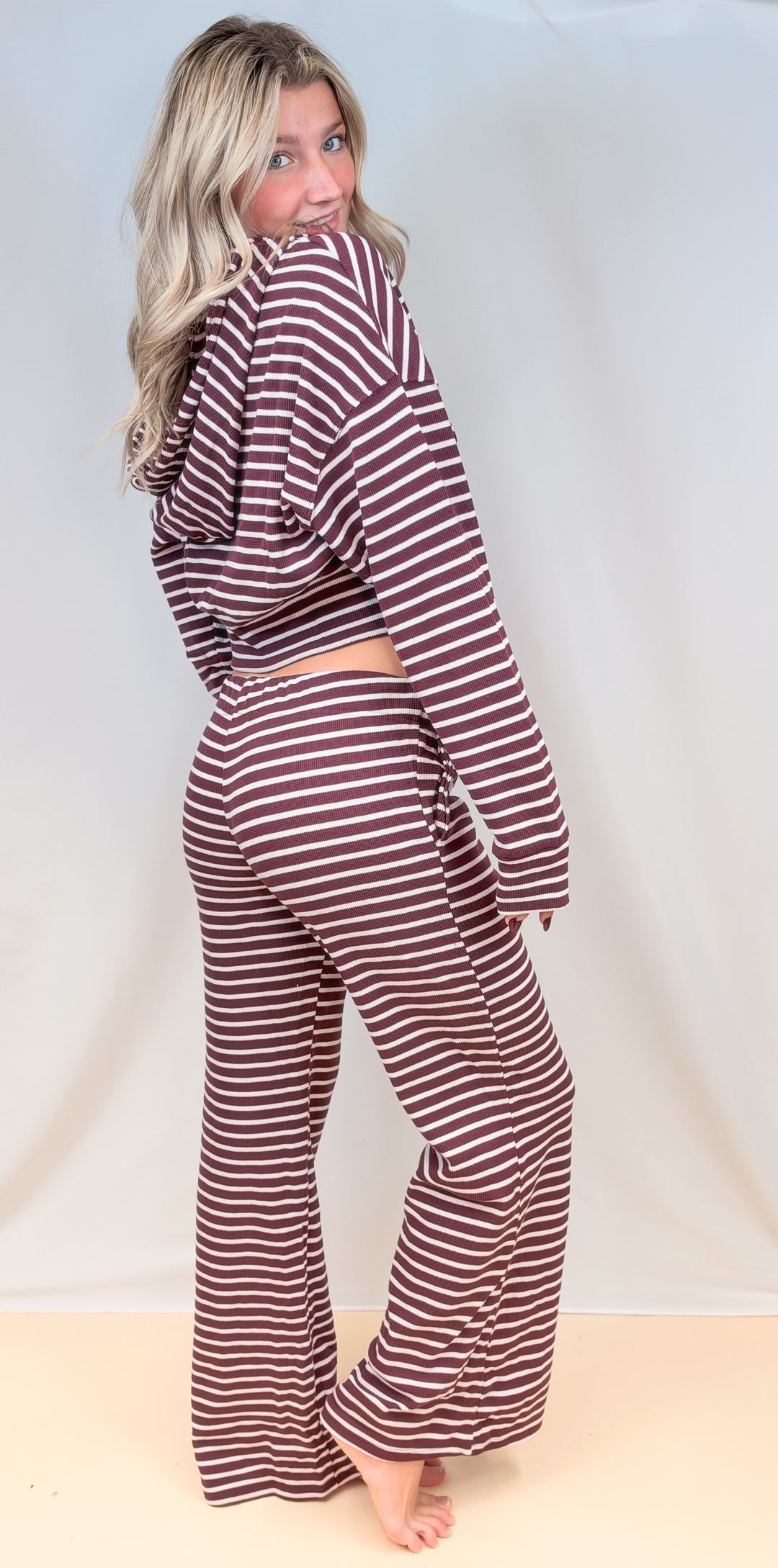 Woman shown from back view wearing matching burgundy and cream stripe set with hoodie and pants on plain background
