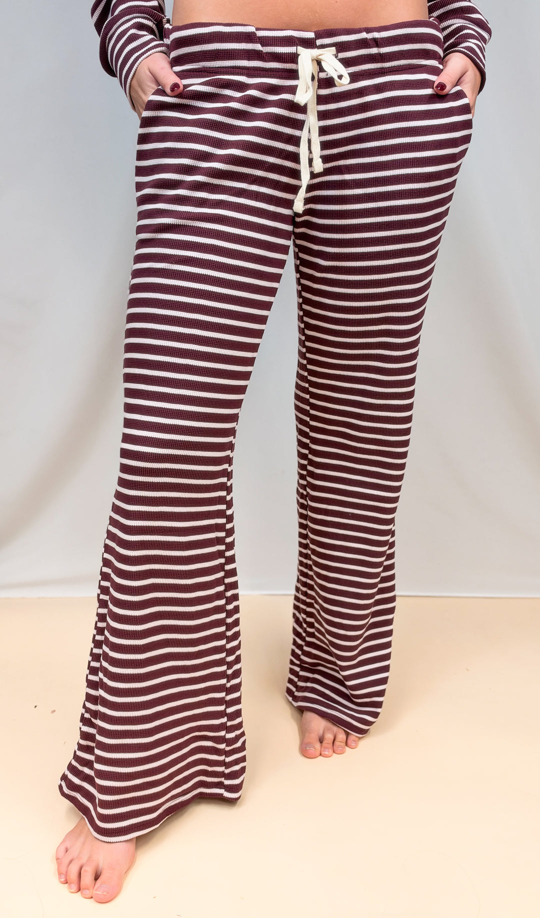 Woman shown waist down wearing burgundy and cream stripe pants on plain background