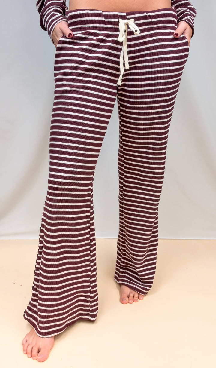 Woman shown waist down wearing burgundy and cream stripe pants on plain background
