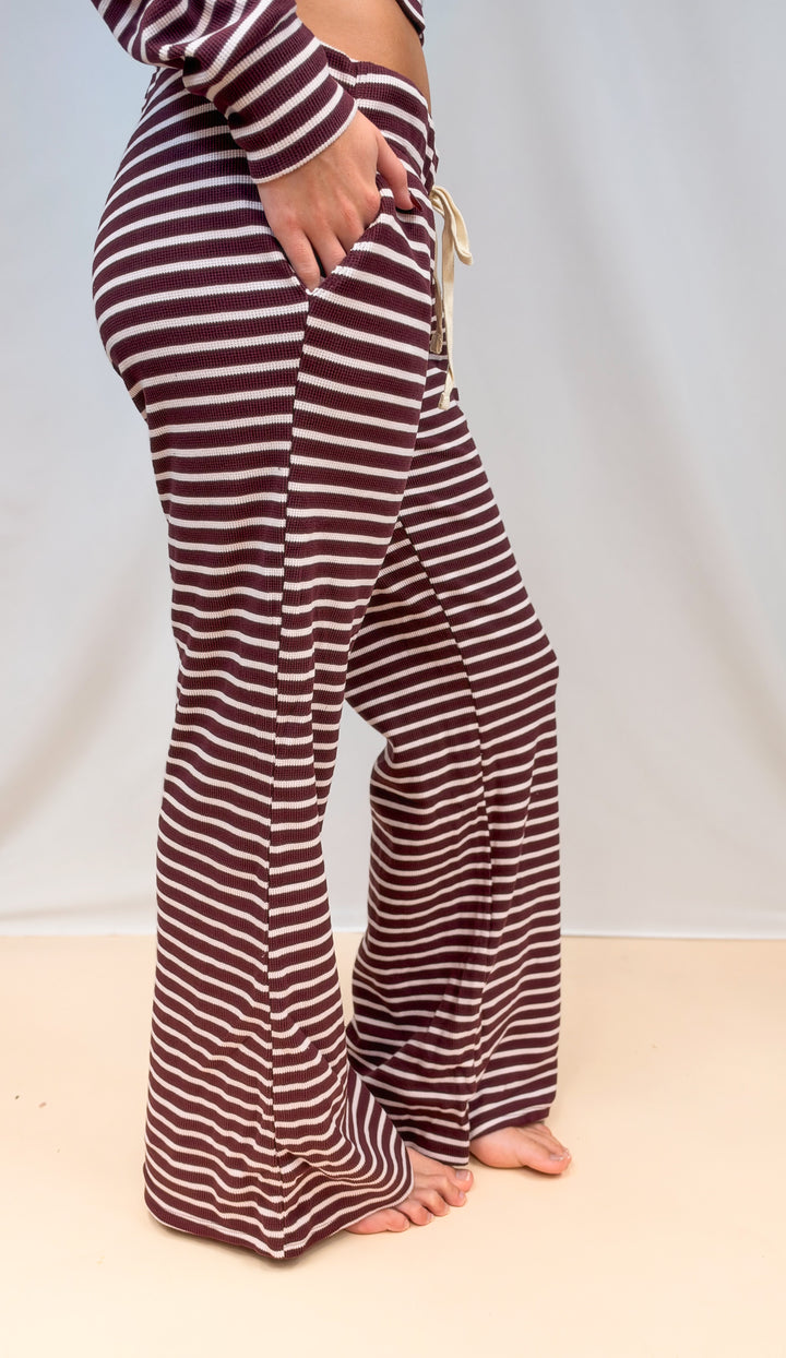 Woman shown waist down from side view wearing burgundy and cream stripe pants on plain background