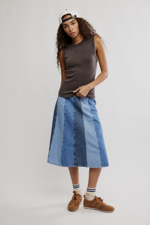 Woman wearing a sleeveless brown top and patchwork denim skirt on a white background