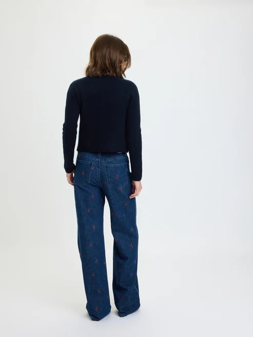 A model viewed from behind wearing a dark navy long-sleeve top and dark blue wide-leg jeans with small red embroidered details, set against a plain white studio background.