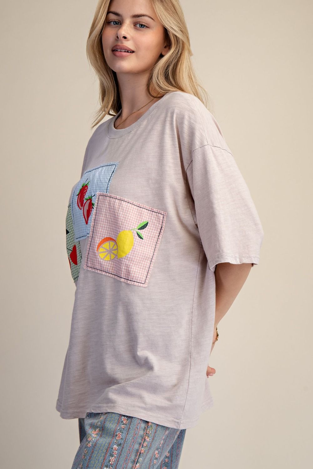 Woman wearing a light gray oversized t-shirt with a colorful graphic design on a plain background