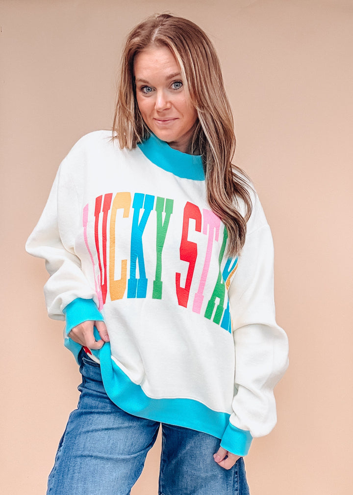 A woman modeling a white crewneck sweatshirt with bright turquoise ribbed trim and a colorful &