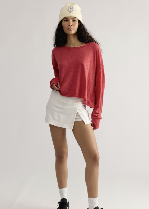 Woman wearing red long sleeve top with white skirt and white beanie on plain background