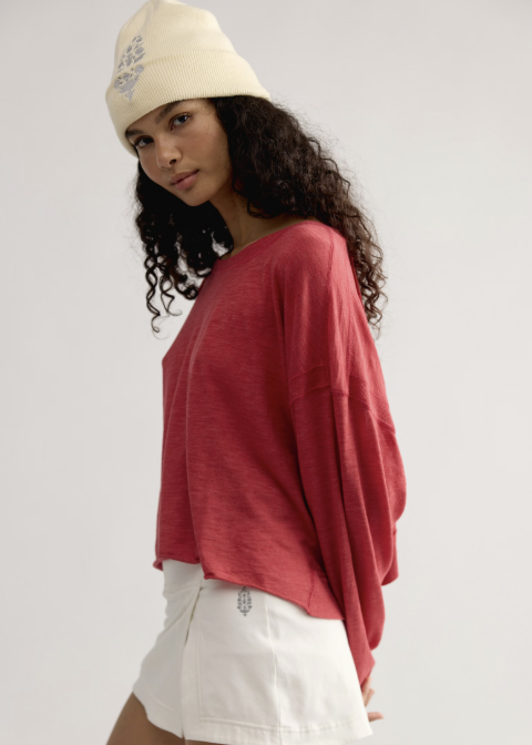 Woman wearing red long sleeve top with white skirt and white beanie on plain background