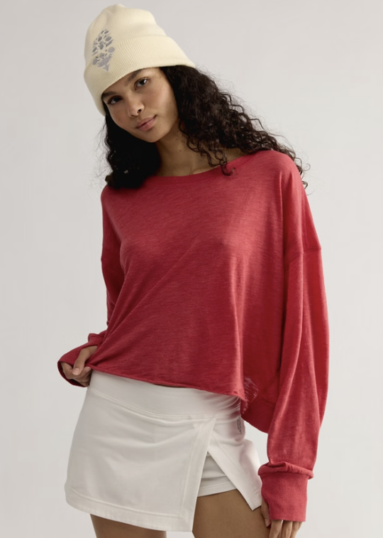 Woman wearing red long sleeve top with white skirt and white beanie on white background