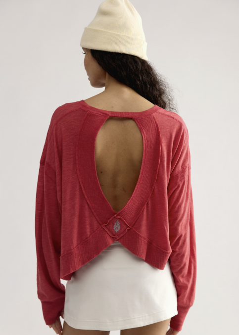 Woman shown from back wearing red long sleeve top with open back detail, white skirt and white beanie on plain background