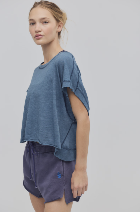 Woman wearing a blue oversized t-shirt and dark shorts on a light gray background