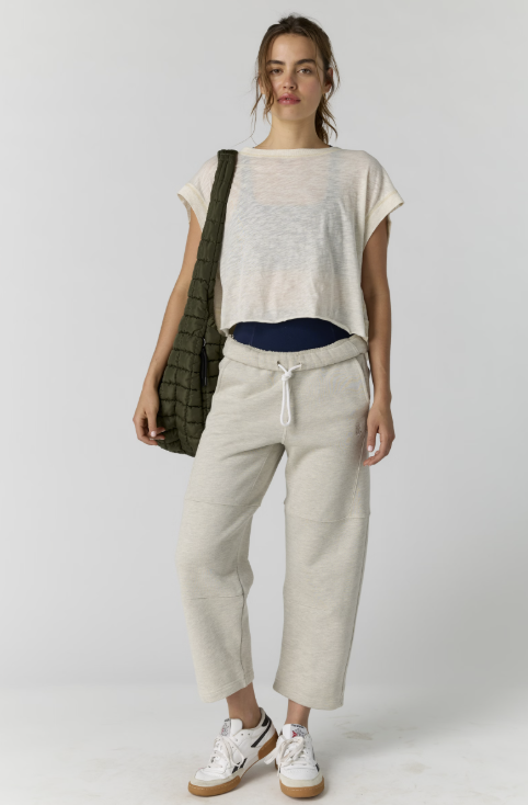 Woman wearing a white top and beige pants with a green bag on a white background