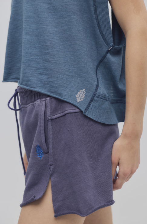 Person wearing a blue shirt and purple shorts with a brand logo on a plain background