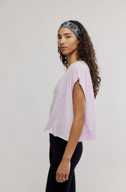 Woman wearing a light purple top and black pants with a patterned headband on a plain background