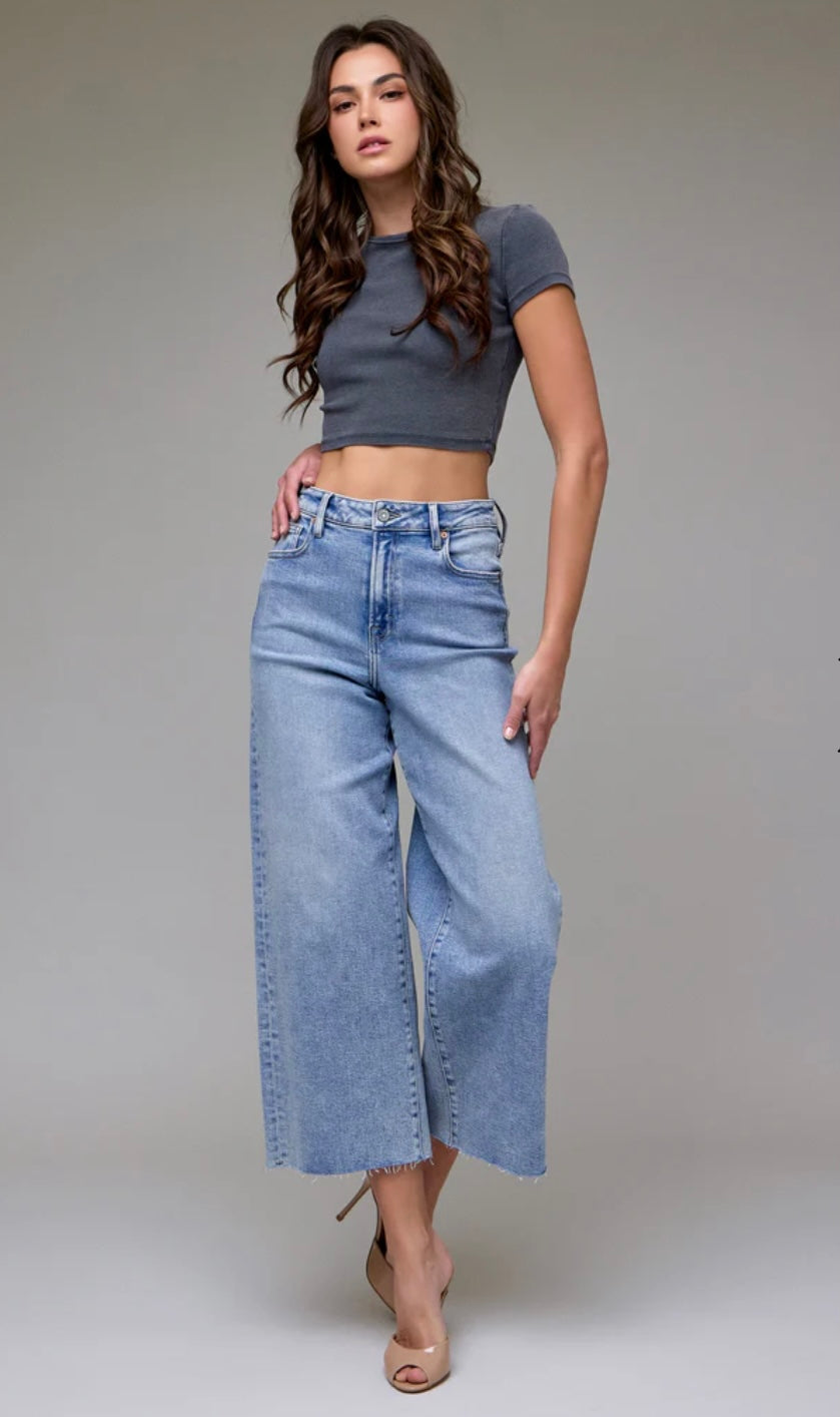 Woman wearing a gray crop top and light blue wide-leg jeans on a plain background