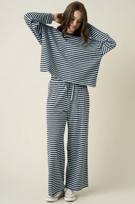 A woman modeling a matching two-piece loungewear set consisting of a long-sleeve cropped top and wide-leg pants, both in a navy and white horizontal stripe pattern, against a plain beige studio background.