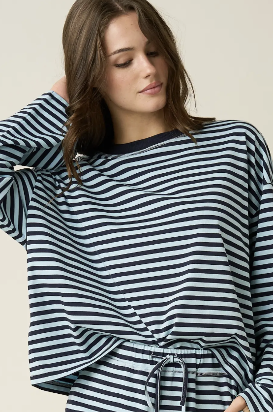 A woman wearing a navy and white horizontally striped long-sleeve top with a drawstring waist, photographed against a plain light beige studio background.