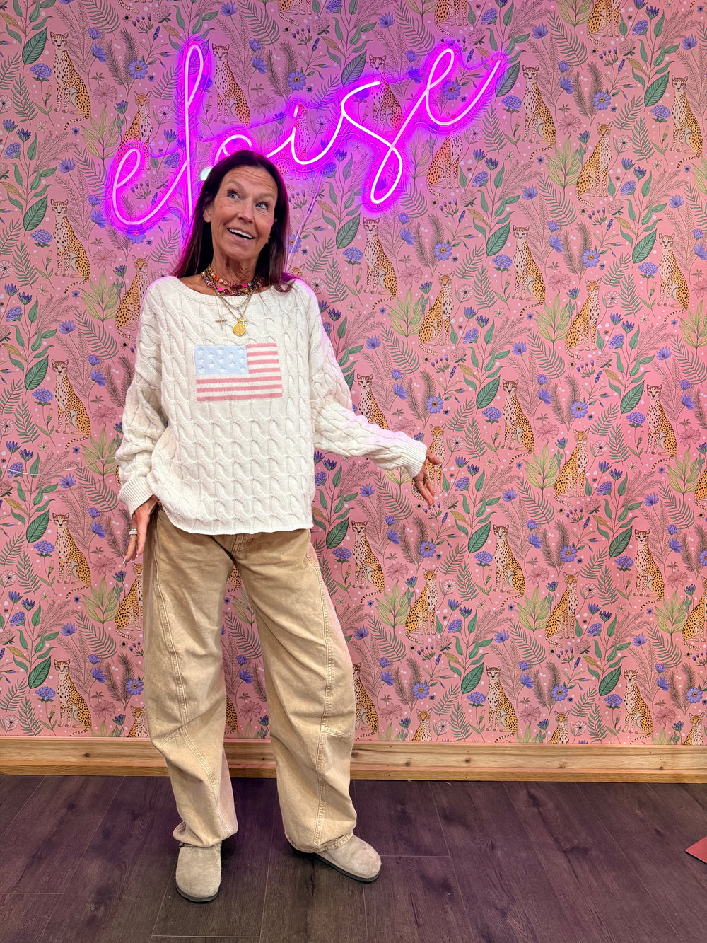 Woman wearing cream sweater with American flag and beige pants on floral background