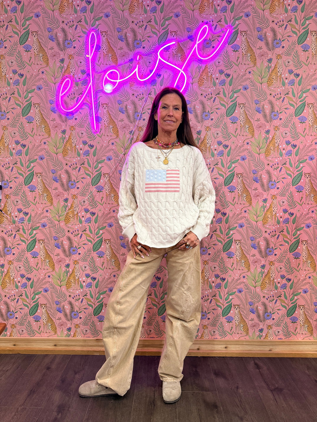 Woman wearing cream sweater with American flag and beige pants on floral background