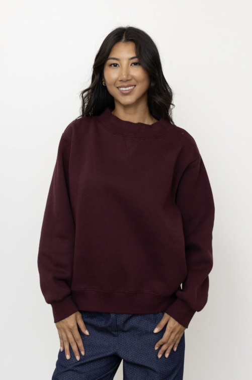 Woman wearing maroon mock neck pullover and jeans on plain background
