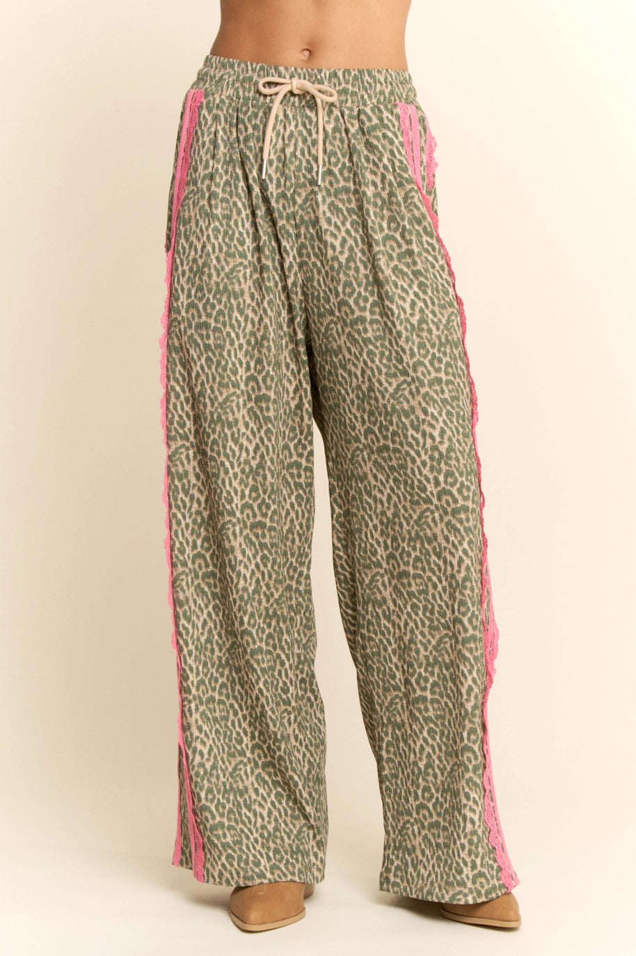 Woman wearing leopard pants with pink lace on sides on plain background