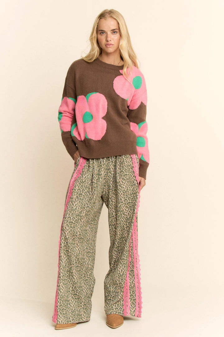 Woman wearing a brown sweater with pink floral patterns and patterned pants on a beige background