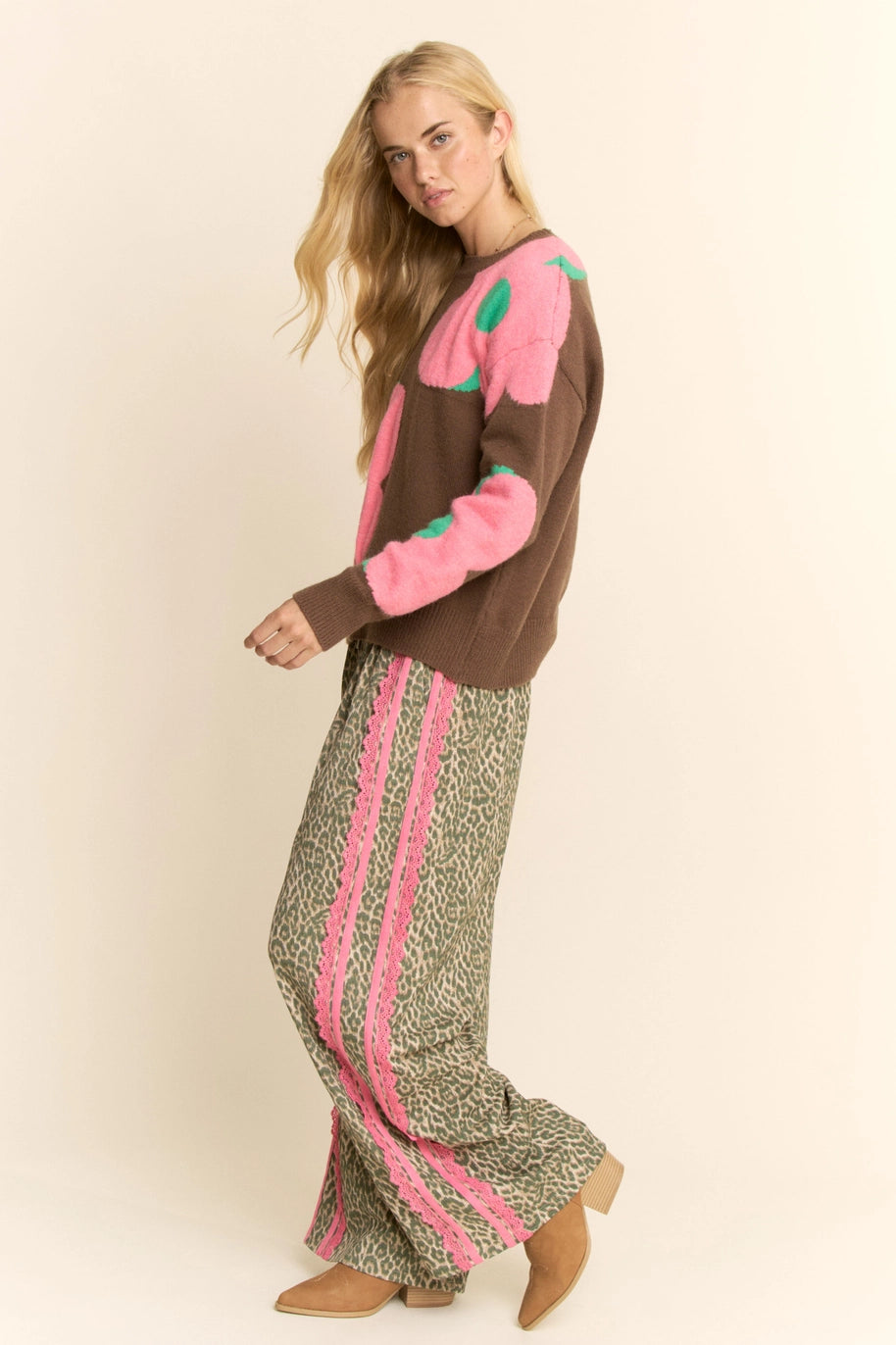 Woman wearing a brown sweater with pink accents and patterned pants on a beige background