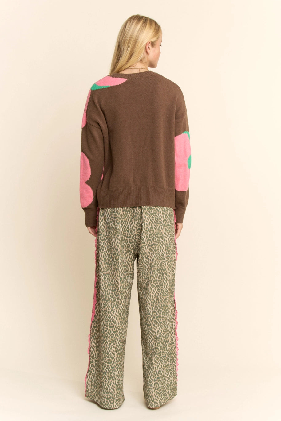 Woman wearing a brown sweater with pink and green accents and patterned pants on a beige background