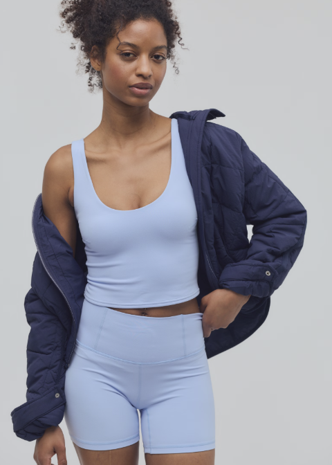 Woman wearing light blue cami and shorts with blue jacket on plain background