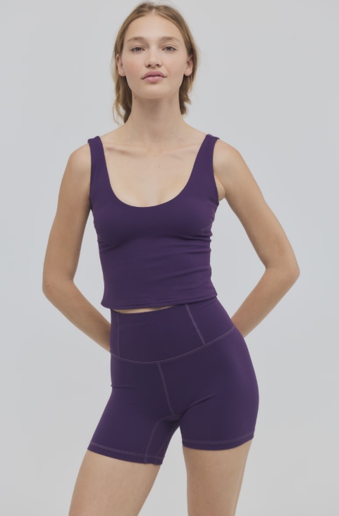 Woman wearing purple cami and bike shorts on plain background