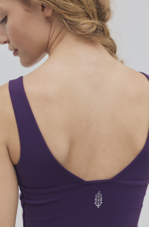 Close up of woman wearing purple cami with logo on back on plain background