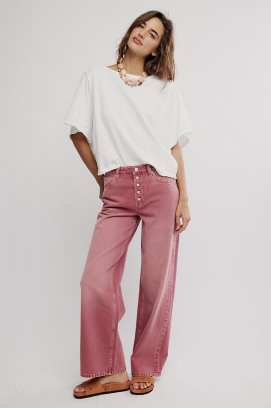 Woman wearing a white top and pink pants on a plain background