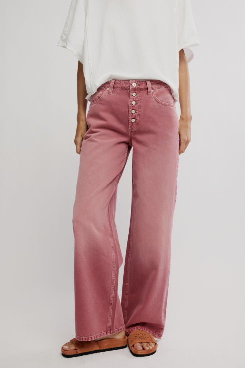 Person wearing pink wide-leg pants with a white top on a plain background